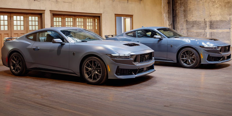 2026 Ford vehicles—two modern sports coupes in a showroom, featuring sleek aerodynamic designs, matte gray and blue finishes, and aggressive front styling.